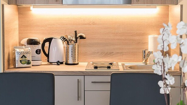 Una cocina moderna con armarios de madera, un horno de acero inoxidable y un bol de manzanas sobre la mesa de comedor.