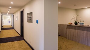 Un pasillo de hotel con una recepción, un cartel que indica los tipos de habitaciones y un cubo de basura.