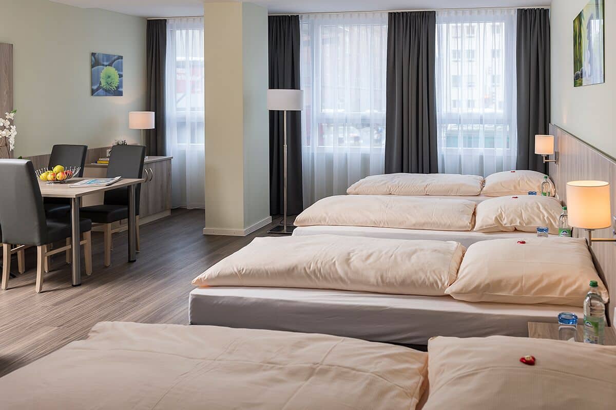 Habitación de hotel con una cama grande, un escritorio con una silla, una lámpara y vistas a la ciudad a través de la ventana.