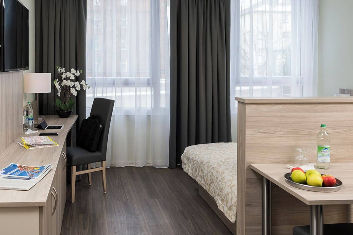 Habitación de hotel con cama, escritorio con silla, televisor, planta y frutero.