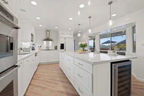 Una cocina moderna con armarios blancos, una isla central y vistas a la montaña a través de amplios ventanales.