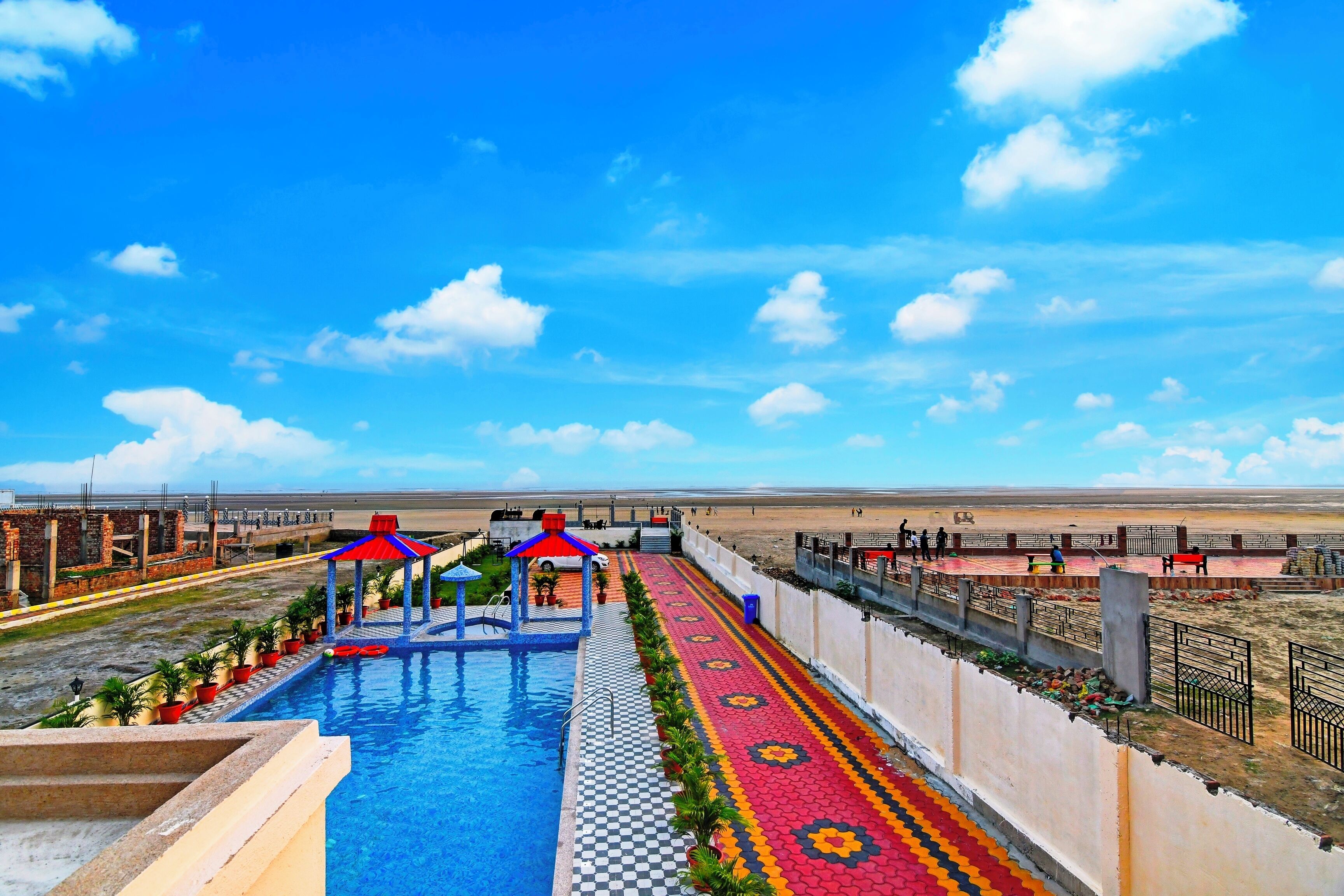Una piscina con diseño a cuadros, un quiosco rojo y azul, y un sendero con diseño.