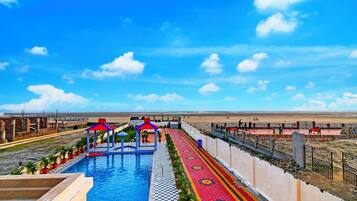 Una piscina con diseño a cuadros, un quiosco rojo y azul, y un sendero con diseño.