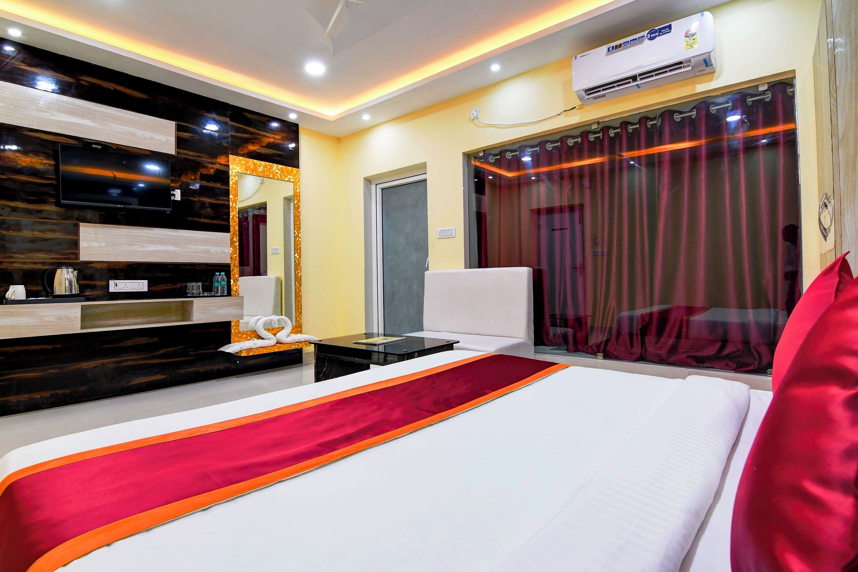 A hotel room with a large bed, a desk, a flat-screen TV mounted on the wall, and an air conditioning unit.