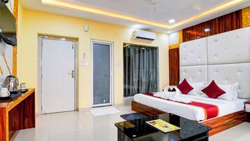 A hotel room with a bed, a coffee table, a desk with a kettle, and an air conditioning unit.