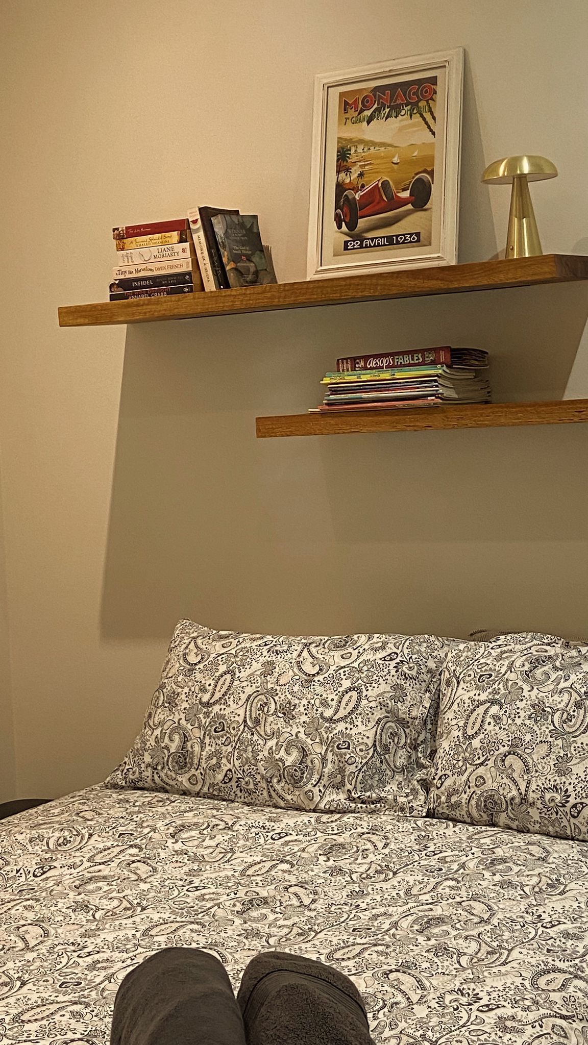 A bedroom with a bed, a patterned pillow, a bookshelf with books and a framed picture, and a lamp.