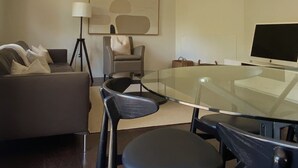 Una sala de estar moderna con una mesa de vidrio, sillas negras, un sofá, una lámpara de pie y un televisor de pantalla plana.