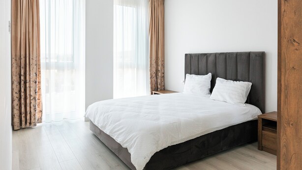 A modern bedroom with a large bed, wooden headboard, and a nightstand.