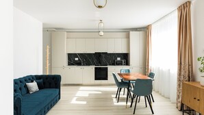 A modern kitchen with white cabinets, a black marble backsplash, and a wooden dining table with blue chairs.
