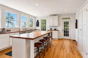 A spacious kitchen with a large island, bar stools, and white cabinetry.
