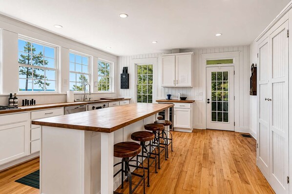 A spacious kitchen with a large island, bar stools, and white cabinetry. - Blackstone on the Bluff | Large Private Beach! (South Haven)
