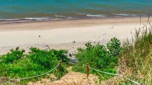 Una playa con agua azul cristalina, orilla de arena y una escalera de madera que baja a la playa.