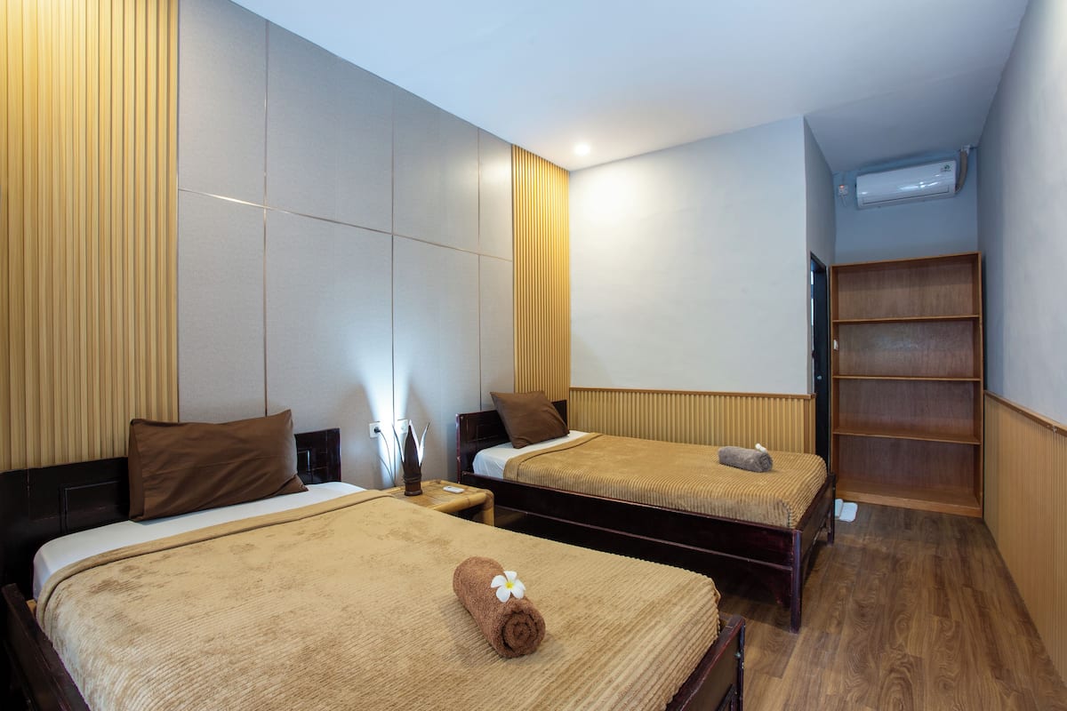 A hotel room with two beds, a wooden floor, a built-in shelf, and an air conditioning unit.