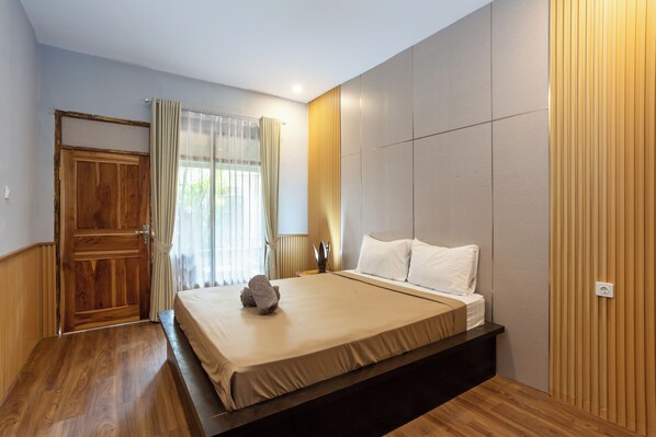 A bedroom with a wooden floor, a bed with white linens, a wooden door, and a window with curtains.