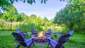 A fire pit with four Adirondack chairs arranged around it in a grassy outdoor area. - The Crescent Cottage | Kayaks | Bonfire | Lakeside (Fennville)