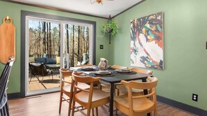 A dining area with a table set for four, surrounded by wooden chairs, a chandelier, and a large abstract painting on the wall. - The Crescent Cottage | Kayaks | Bonfire | Lakeside (Fennville)