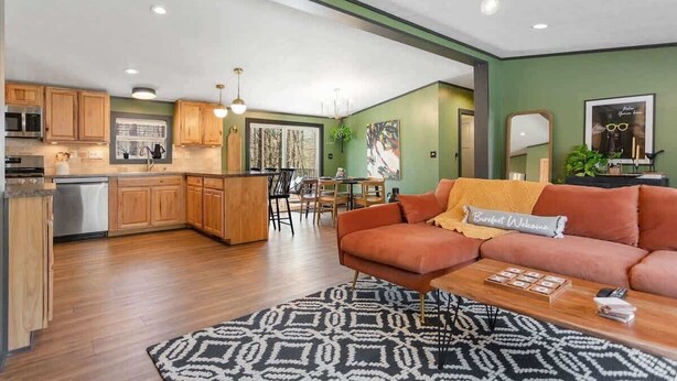 A modern kitchen with wooden cabinets, a dining area with a table and chairs, and a living room with a sofa and coffee table. - The Crescent Cottage | Kayaks | Bonfire | Lakeside (Fennville)