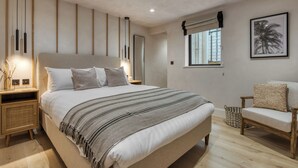 Een moderne slaapkamer met een groot bed, nachtkastjes, een stoel, een raam met uitzicht en een ingelijste foto aan de muur.