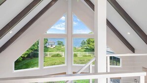 A high-ceilinged room with large windows offering a view of a well-maintained lawn and a distant house.