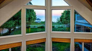 A multi-level room with large windows offering views of a garden, a gazebo, and a blue building.