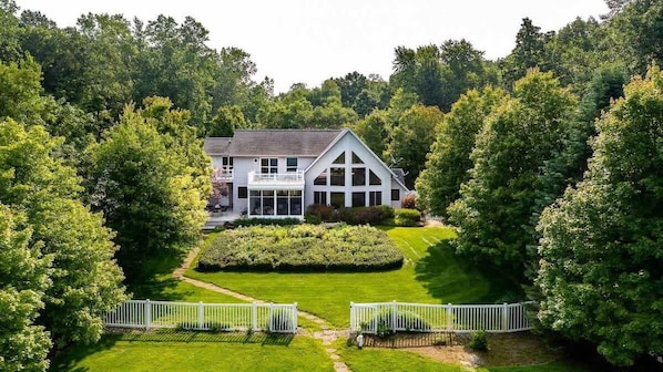 A large house surrounded by lush greenery, with a well-maintained lawn and a white fence.