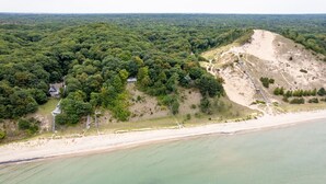Oversigtsbillede af et kystområde med strand, skovklædte bakker og et hus med veranda.