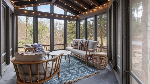 Une véranda avec un ventilateur de plafond, des guirlandes lumineuses, un canapé, des fauteuils et une petite table.