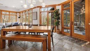 Un vaste espace dédié à la salle à manger, avec une table et des bancs en bois, de grandes fenêtres et une vue sur l’extérieur.