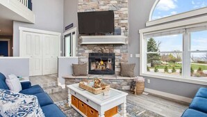 A modern living room with a stone fireplace, a flat-screen TV, and a large window offering a view of the outdoors.
