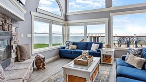 A spacious living room with a stone fireplace, a blue sofa set, and large windows offering a view of the ocean.