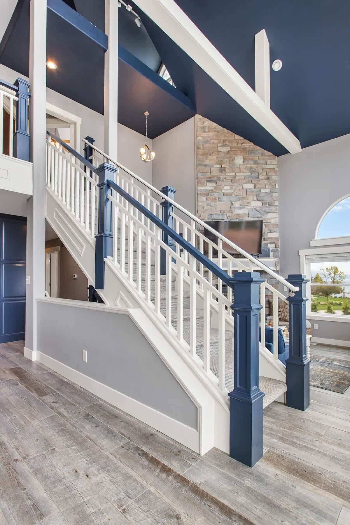 Un intérieur spacieux avec un magnifique escalier, une cheminée en pierre et une vue dégagée sur l’extérieur grâce à une grande fenêtre.