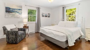 A bedroom with a bed, a chair, a ceiling fan, and a window with curtains. - Woodcliff Cottage | Pool | Bonfire | Coffee Bar (Holland)
