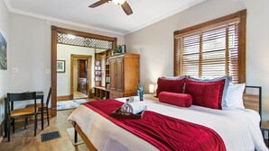 A bedroom with a large bed, a ceiling fan, wooden blinds, and a bookshelf. - Chateau d'Vine | Beautiful Victorian Farmhouse! (Douglas)