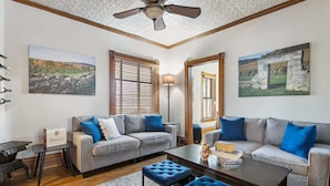 A living room with two grey sofas, blue cushions, a wooden coffee table, and a ceiling fan. - Chateau d'Vine | Beautiful Victorian Farmhouse! (Douglas)