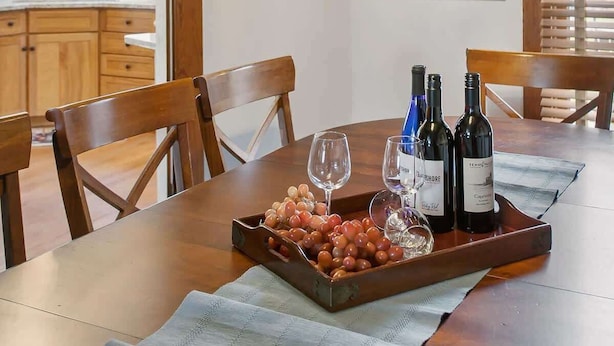 A dining area with a wooden table, chairs, a chandelier, and a tray with grapes and wine bottles. - Chateau d'Vine | Beautiful Victorian Farmhouse! (Douglas)