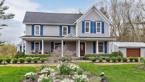 A two-story house with a front porch, a garage, and a well-maintained garden with flowers and shrubs. - Chateau d'Vine | Beautiful Victorian Farmhouse! (Douglas)