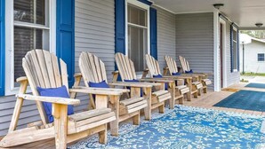 A row of wooden Adirondack chairs with blue cushions on a porch with a patterned rug. - Chateau d'Vine | Beautiful Victorian Farmhouse! (Douglas)
