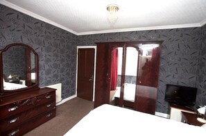 A bedroom with a large bed, a dresser, a television, and a wardrobe.