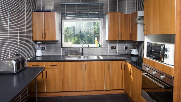 Una cocina moderna con armarios de madera, encimera negra, horno integrado y ventana con vistas a zonas verdes.