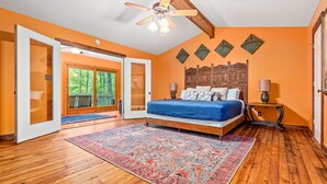 A bedroom with a large bed, a ceiling fan, a wooden floor, and a view of the outdoors through a glass door. - Serene Lakefront Home: Private Dock, Expansive Decks, Game Room & Nature Views (LaGrange)