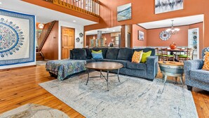 A spacious living room with a large sectional sofa, a round coffee table, and a staircase leading to an upper level. - Serene Lakefront Home: Private Dock, Expansive Decks, Game Room & Nature Views (LaGrange)