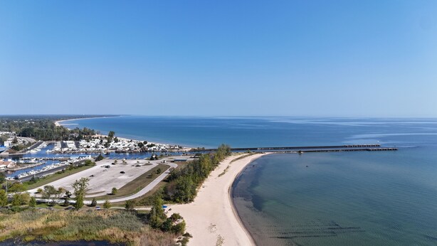 Un pueblo costero con un puerto deportivo, una playa de arena y un muelle largo que se adentra en el mar.