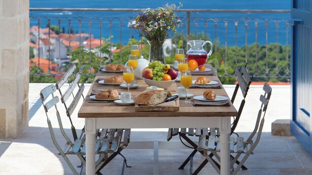 Een ontbijttafel met uitzicht op zee, een stenen boog en een blauwe deur.