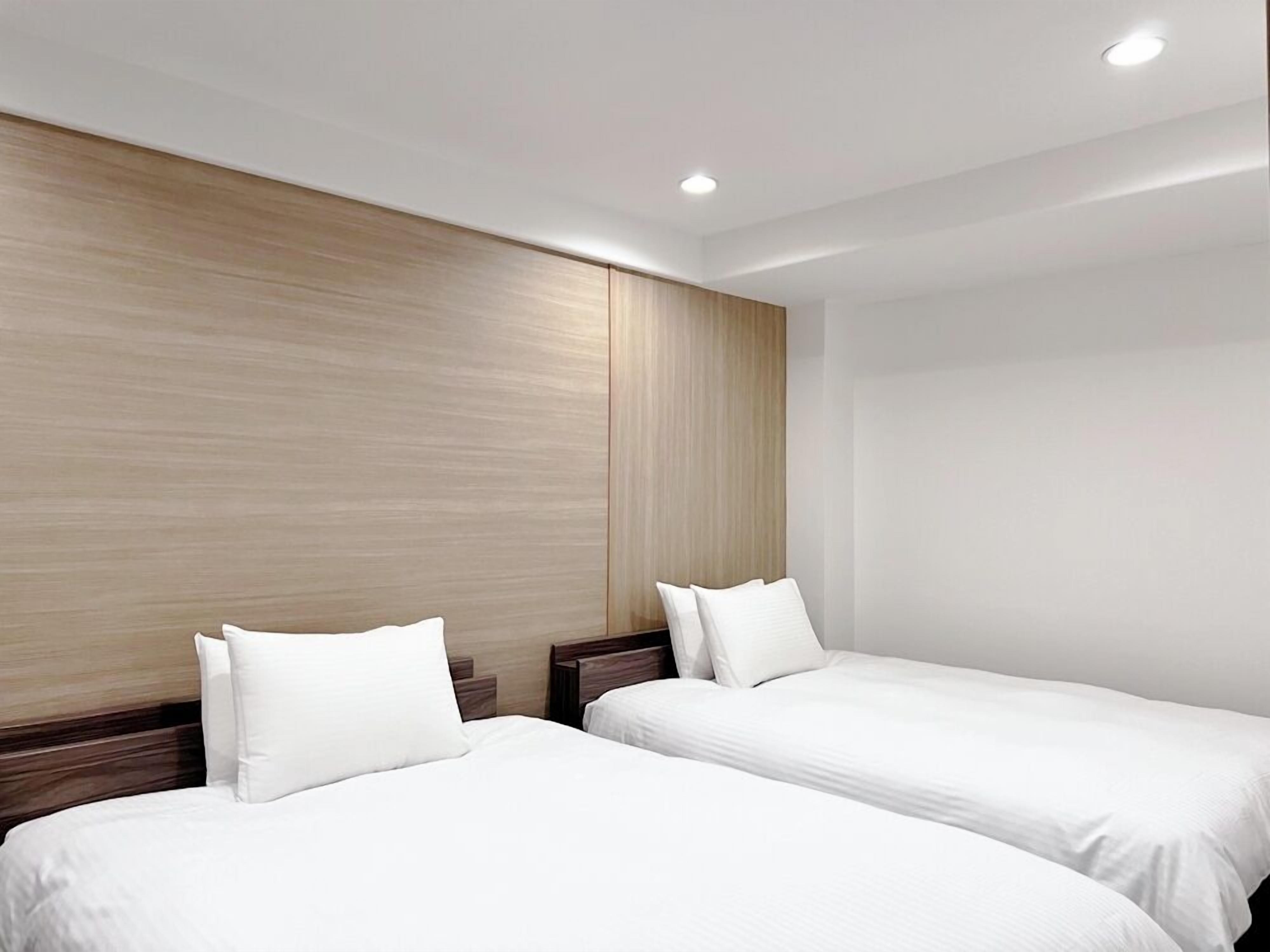 A hotel room with two beds, wooden headboards, and recessed ceiling lighting.