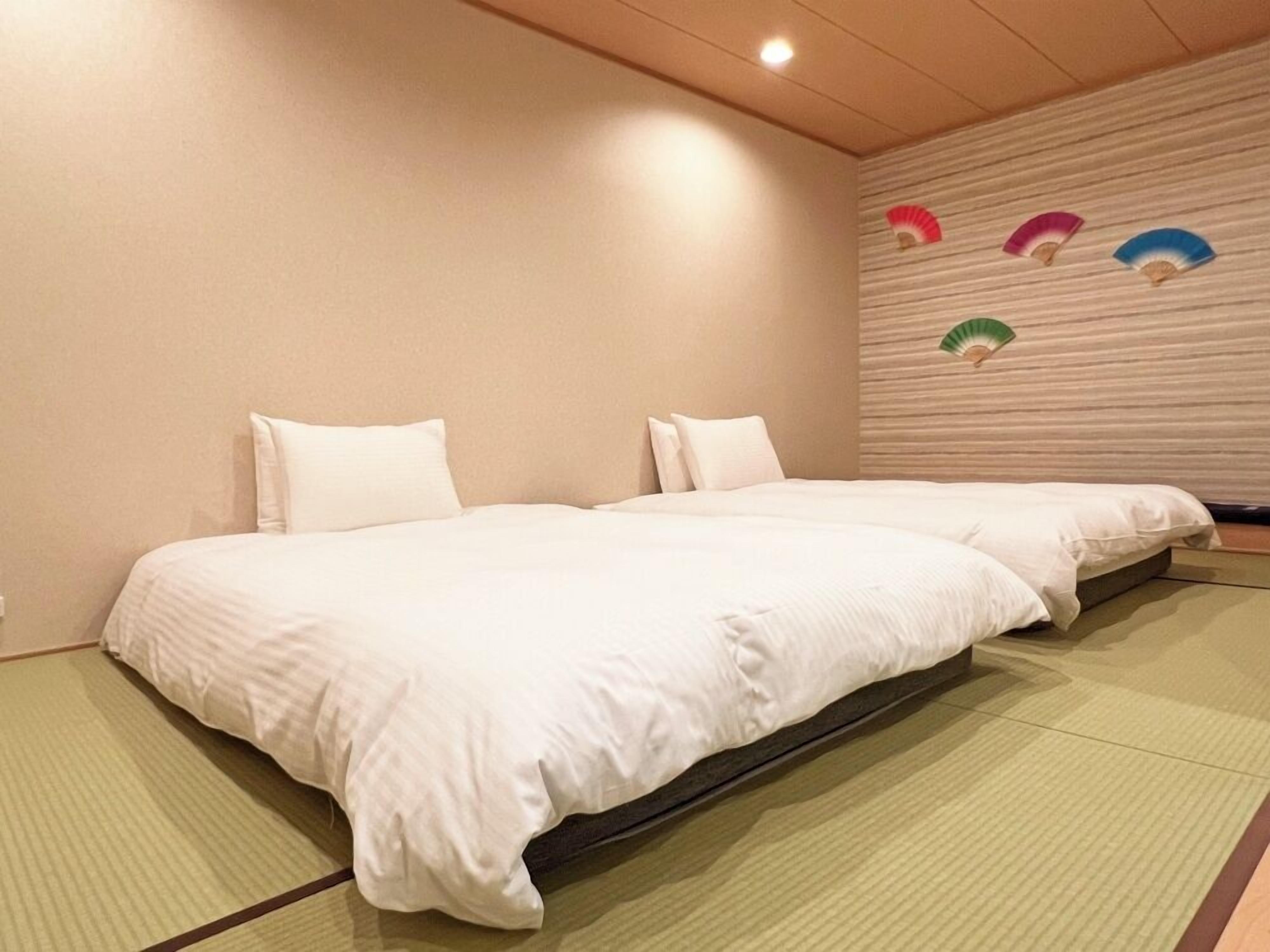 A room with two beds, a tatami mat floor, and a wall with decorative fans.
