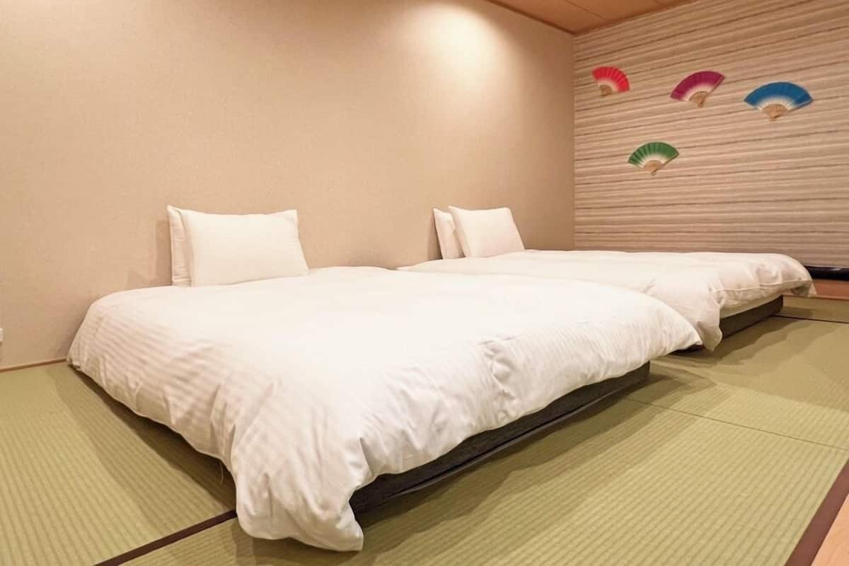A room with two beds, a tatami mat floor, and a wall with decorative fans.
