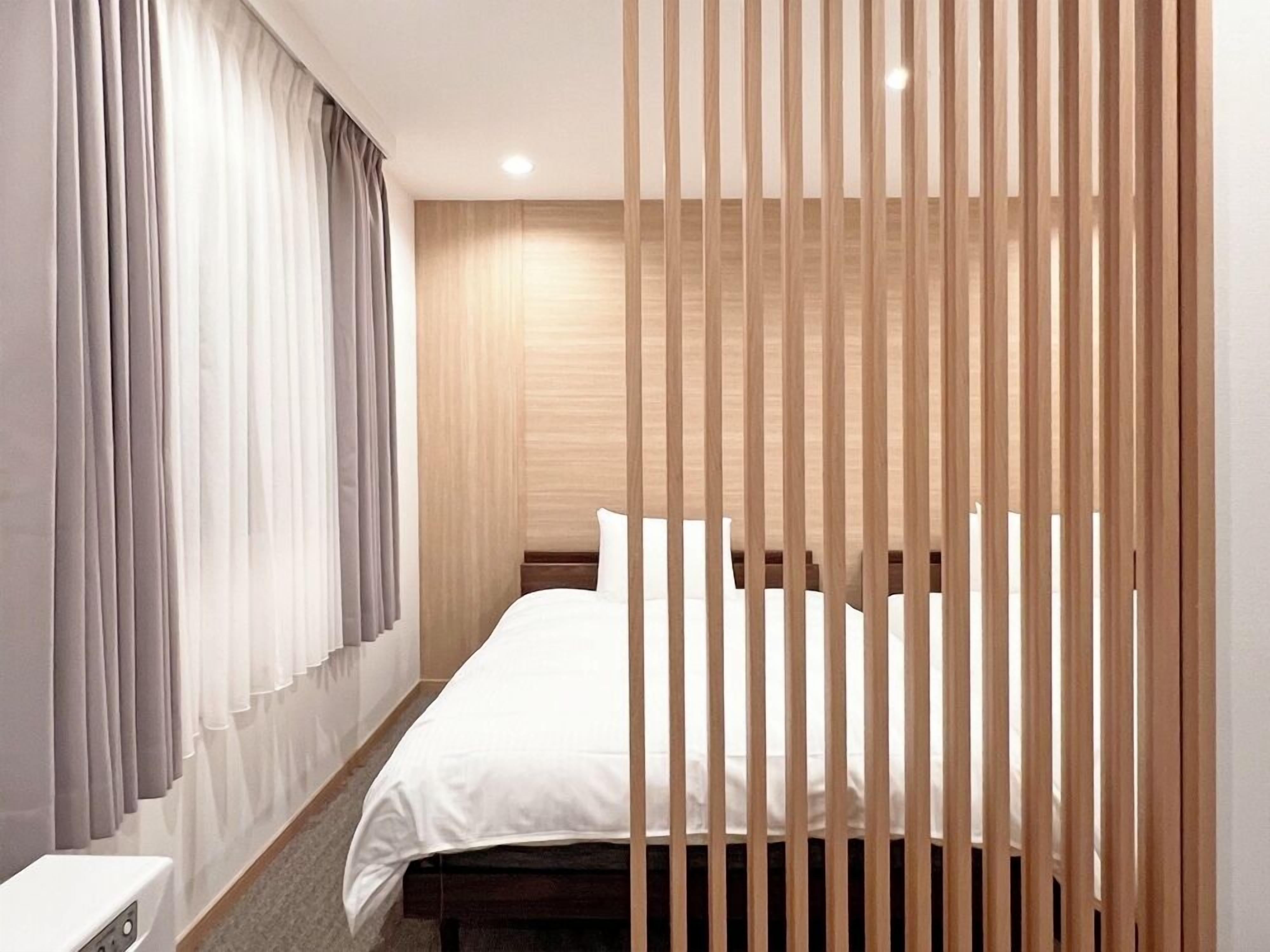 A modern hotel room with a bed, curtains, and a wooden partition.