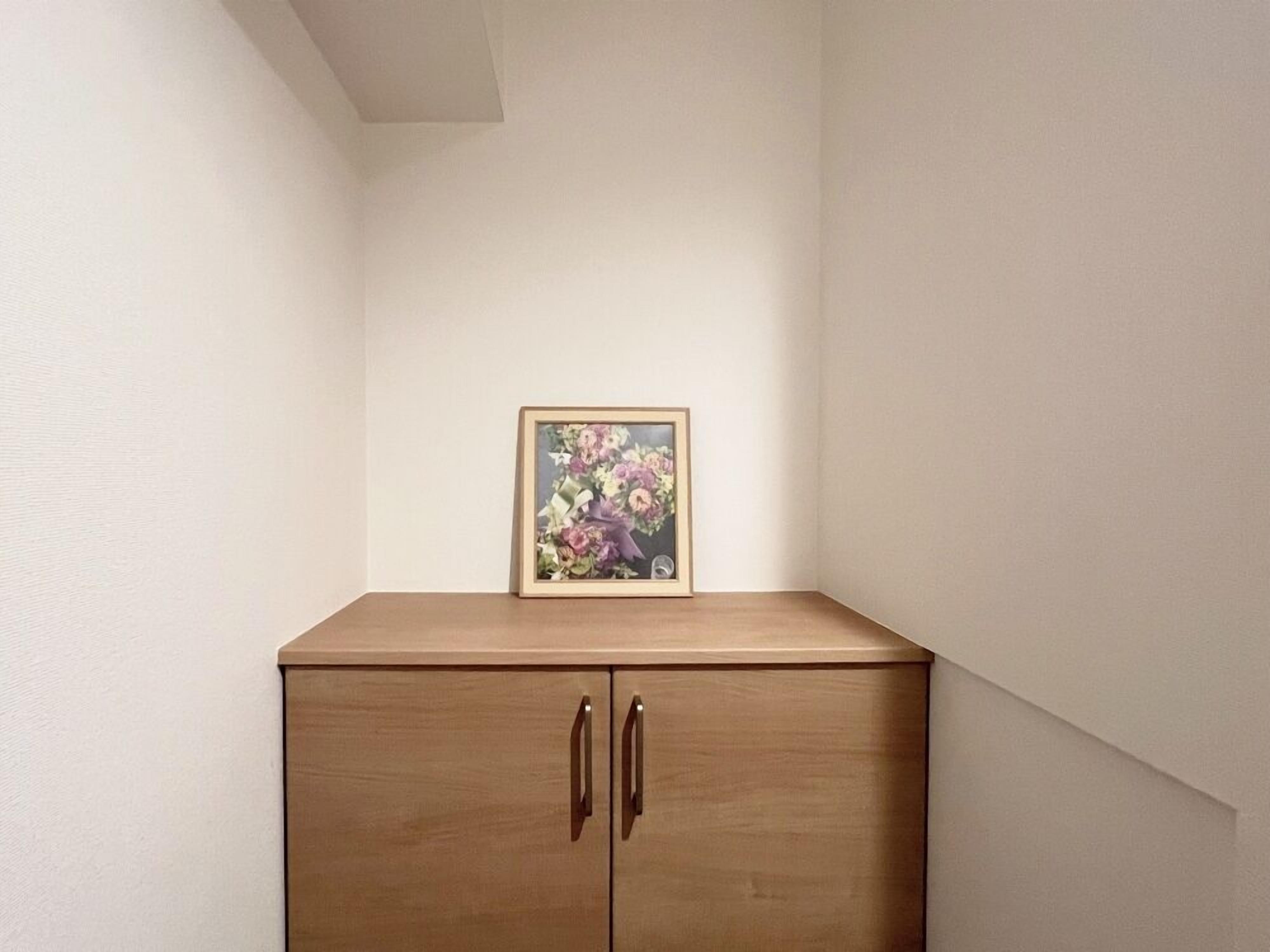 A wooden cabinet with two doors and a framed picture of flowers on top.