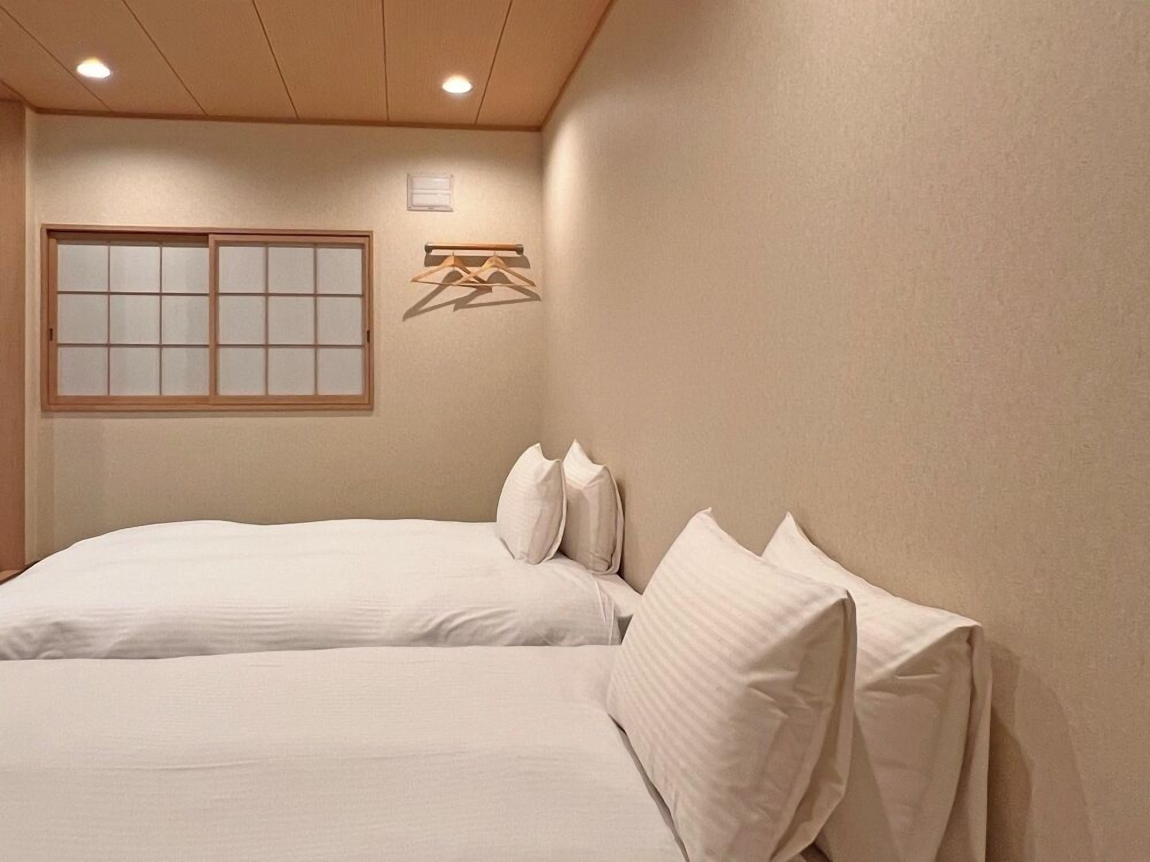 A hotel room with two beds, a shoji screen, and a wooden ceiling.