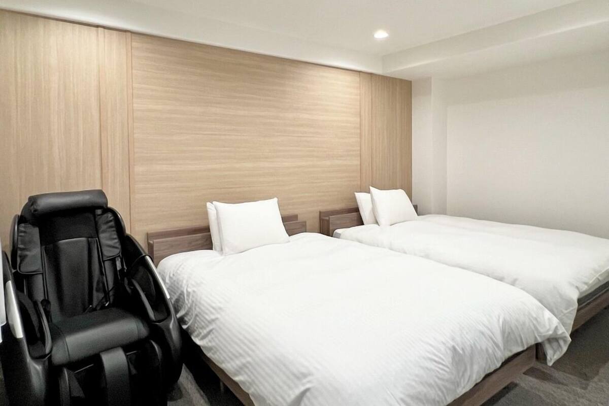 A hotel room with two beds, a massage chair, and a wooden accent wall.
